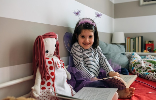 Niña disfrazada de mariposa leyendo con su muñeca