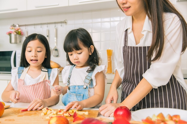 Niña disfruta jugando cortar manzana junto con la madre y la hermana en la cocina de casa.