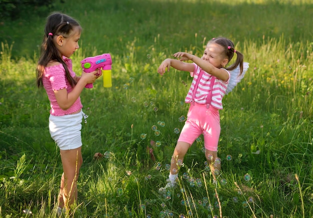 Foto una niña dispara pompas de jabón con una pistola a su graciosa hermana menor que se ríe