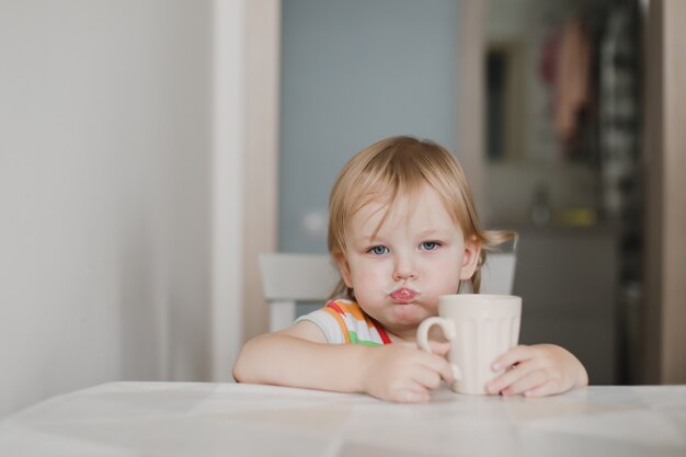 Niña divertida bebiendo leche sentado en la cocina