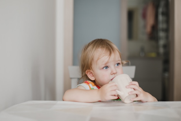 Foto niña divertida bebiendo leche sentado en la cocina