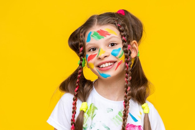 Foto niña divertida con una cara pintada con pinturas coloridas infancia feliz fondo amarillo aislado
