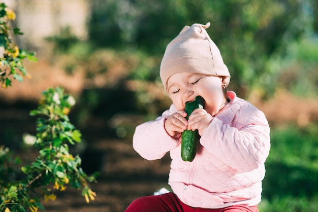 Niña divertida comiendo pepino fresco en el jardín en primavera