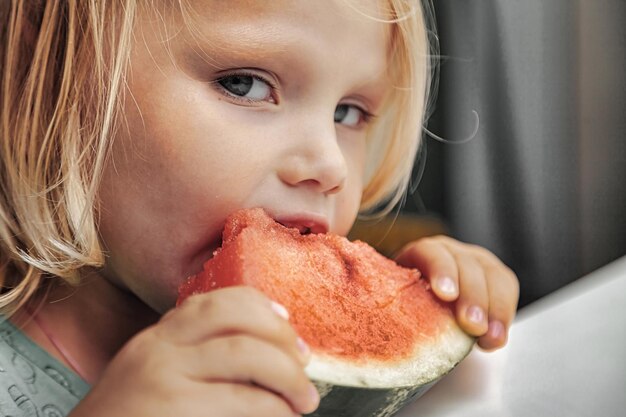 Niña divertida comiendo primer plano de sandía. Niño lindo con sandía en el interior. Concepto de comida sana, verano. Copia espacio