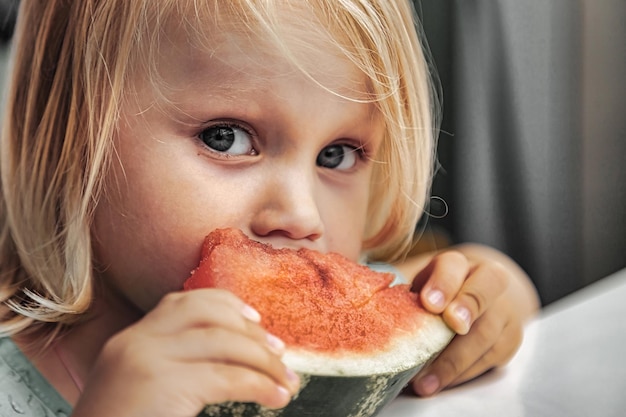 Niña divertida comiendo primer plano de sandía. Niño lindo con sandía en el interior. Concepto de comida sana, verano. Copia espacio