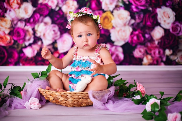 Niña divertida con corona de flores posando en la cesta en la decoración de flores en el estudio