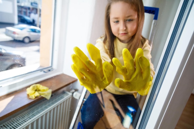 Niña divertida en las escaleras con guantes amarillos lavando la ventana