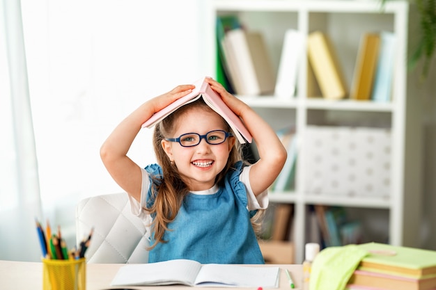 Niña divertida con gafas y libro sobre su cabeza