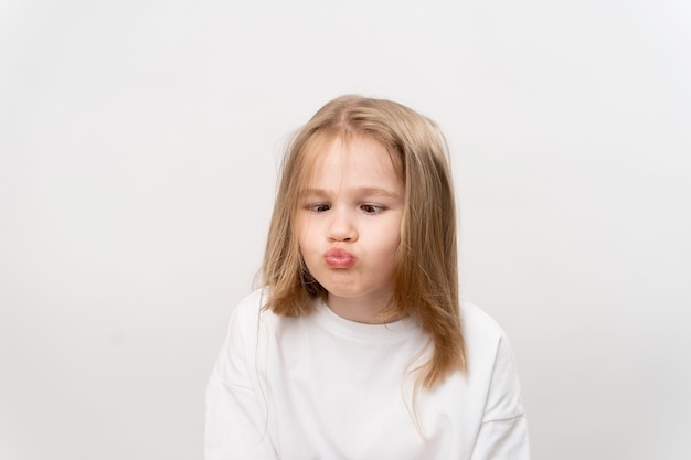 Niña divertida hace muecas sobre un fondo blanco. infancia feliz. vitaminas y medicinas para el niño.