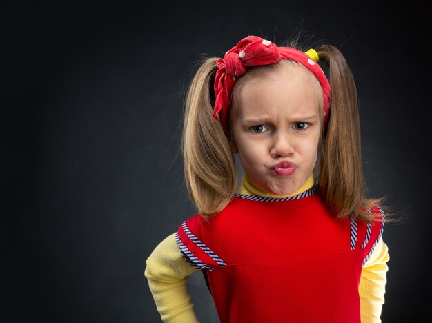 Niña divertida haciendo muecas sobre superficie gris