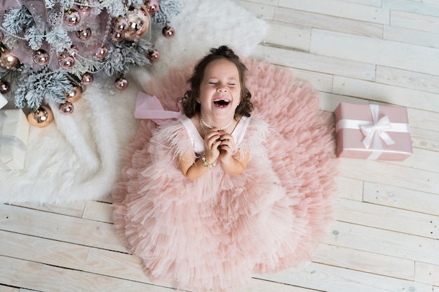 Niña divertida con un hermoso vestido está feliz con regalos para Navidad.