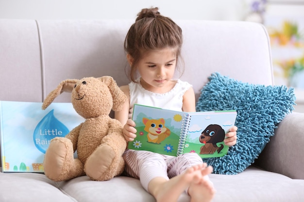 Niña divertida leyendo un libro en el sofá de casa