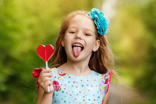 Niña divertida con piruletas en forma de corazón, mostrando su lengua.