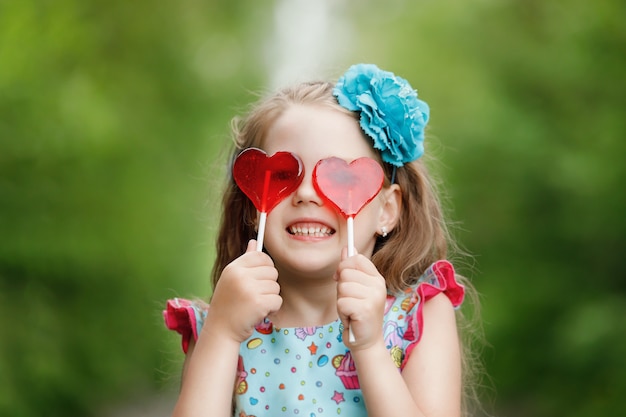 Niña divertida con piruletas en forma de corazón, muestra sus dientes blancos.