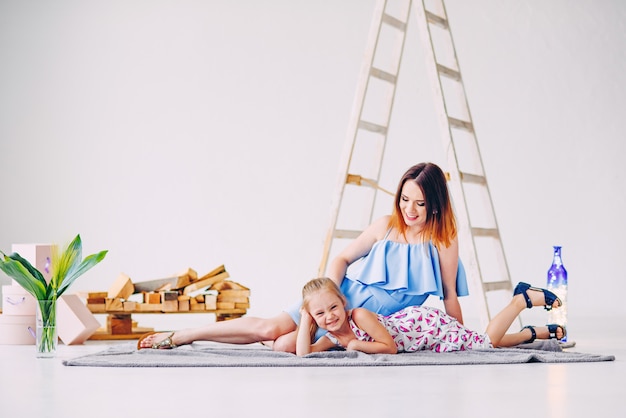 Niña divertida que se divierte con su madre en la habitación blanca decorada. Copia vacía, espacio libre para texto.