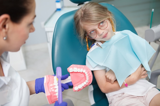 Niña divertida que parece molesta, poniendo los ojos en blanco mientras su dentista la educa sobre la higiene de los dientes