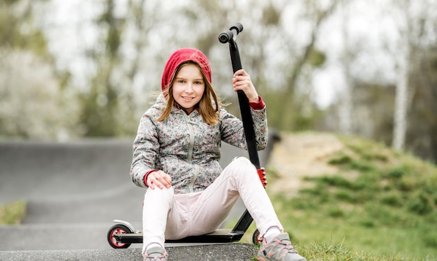 Foto niña divertida con un scooter en un parque de atracciones extremas sonriendo y mirando a la cámara