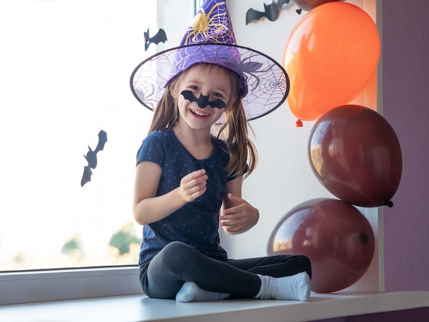 Una niña divertida sonriendo con un sombrero de bruja se pegó un bate en la nariz riéndose Feliz Halloween