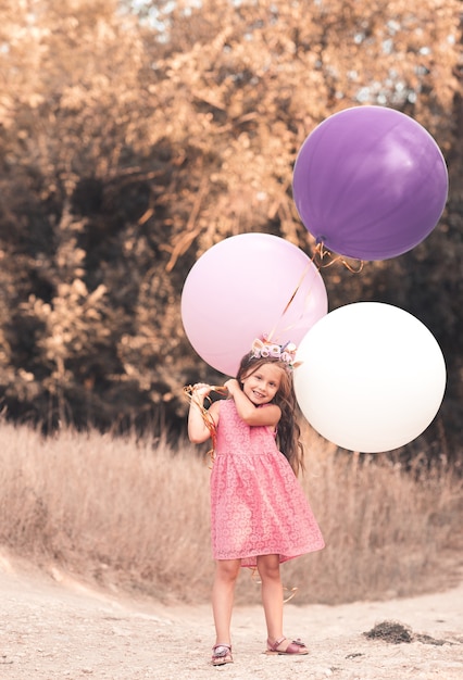 Niña divertida sosteniendo globos de colores en el parque