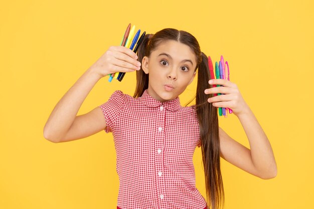 Niña divertida sostiene bolígrafos o marcadores coloridos para estudiar en la escuela