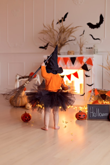 Niña divertida en traje de bruja de halloween con calabaza y escoba en el interior