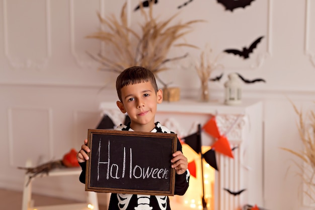 Foto niña divertida en traje de esqueleto de halloween con calabaza y escoba en el interior