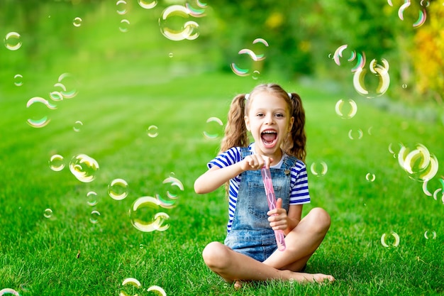 Niña divertida en el verano en el césped con pompas de jabón en la hierba verde divirtiéndose y regocijándose espacio para el texto