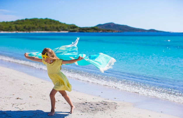 Niña divertirse con una toalla de playa durante las vacaciones tropicales