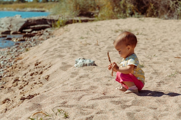 La niña se divierte y juega con un palo en la playa de arena a la luz del sol