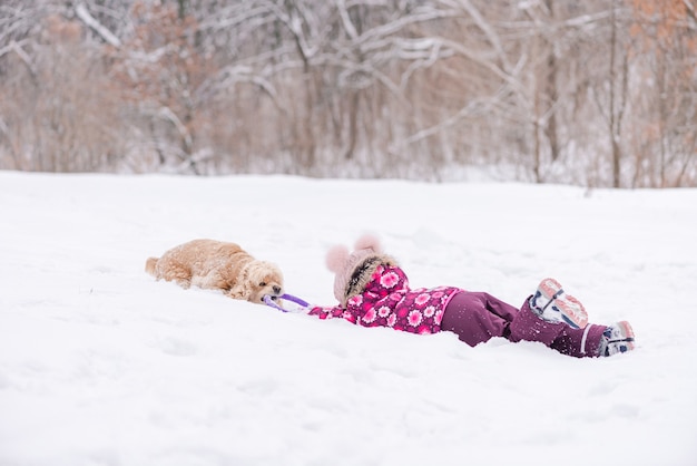 Niña divirtiéndose con cocker spaniel en invierno. Niño femenino con perro jugar con juguete de anillo en la nieve
