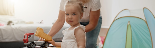 Niña divirtiéndose con mamá en la sala de juegos en casa y mirando la cámara