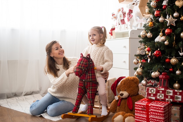 Niña divirtiéndose con su madre en casa cerca del árbol de Navidad