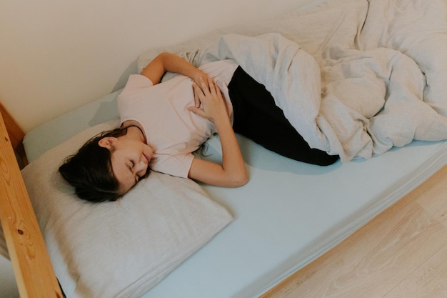 Niña dormida en la cama con dolor de estómago