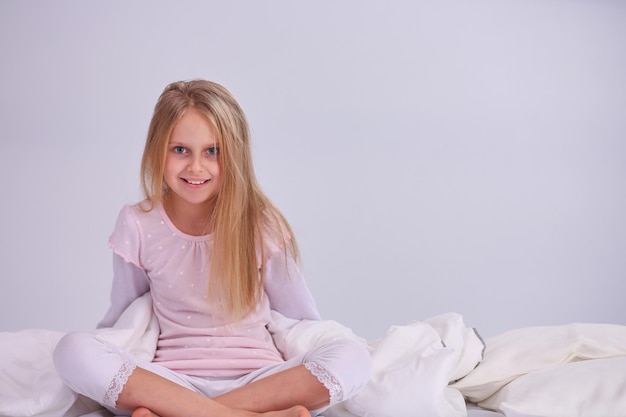 La niña en el dormitorio está sentada en la cama La niña lleva un pijama y está sentada en la cama