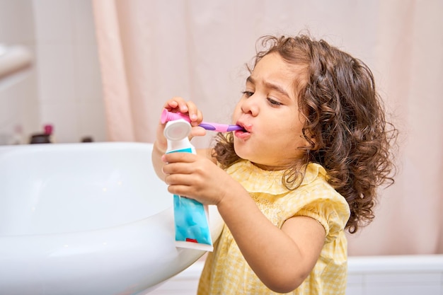 Niña de dos años cepillándose los dientes sola en el baño de casa.