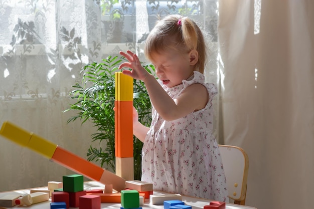 Foto una niña de dos años está sentada en una mesa y ensambla un kit de construcción de madera un niño rompe una torre de cubos