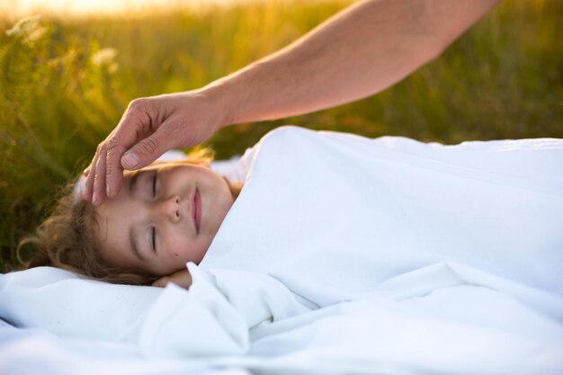 La niña duerme en una cama blanca en el aire fresco de la hierba. La mano de papá le da palmaditas en la cabeza. Protección del cuidado. Picaduras de mosquitos del Día Internacional del Niño.