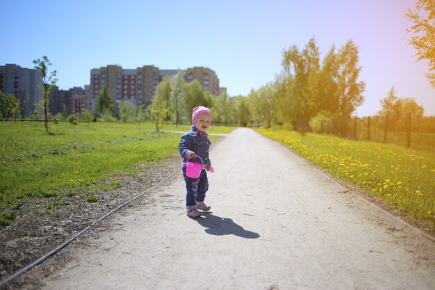 Una niña dulce, con un balde de arena rosa, camina en un hermoso parque de verano