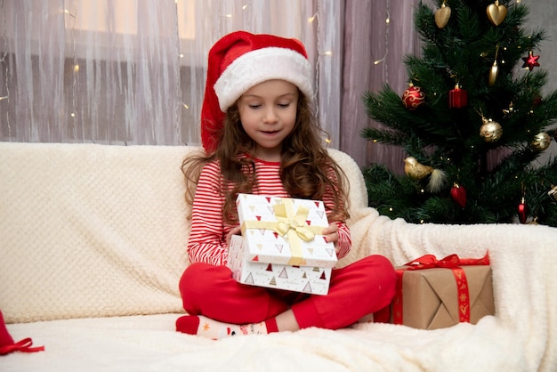 Una niña dulce en el sombrero de Santa con regalos cerca del árbol de Navidad Casa de Año Nuevo de Navidad