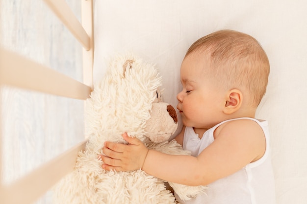 Niña durmiendo en una cama blanca con un oso suave, sueño saludable para bebés