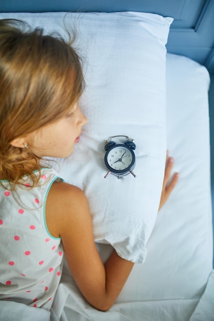 Niña durmiendo en una cama grande y acogedora ropa blanca por la tarde en casa