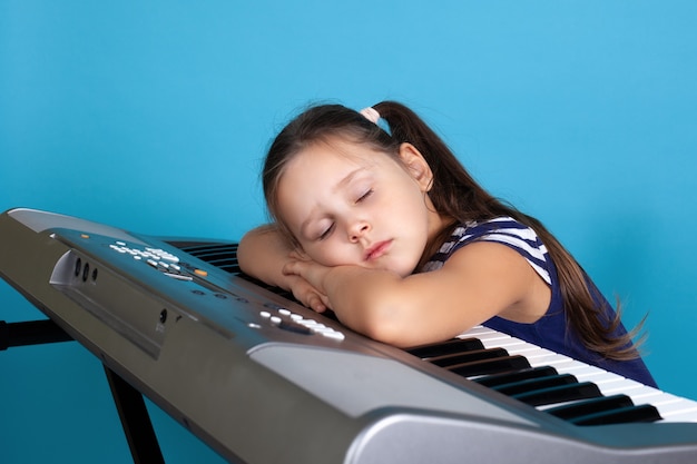 Niña durmiendo en las teclas de un sintetizador electrónico, cansada en la escuela de música