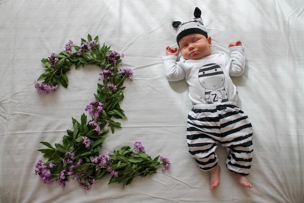 Niña durmiendo en un traje de cebra junto a flores lilas en forma de número dos