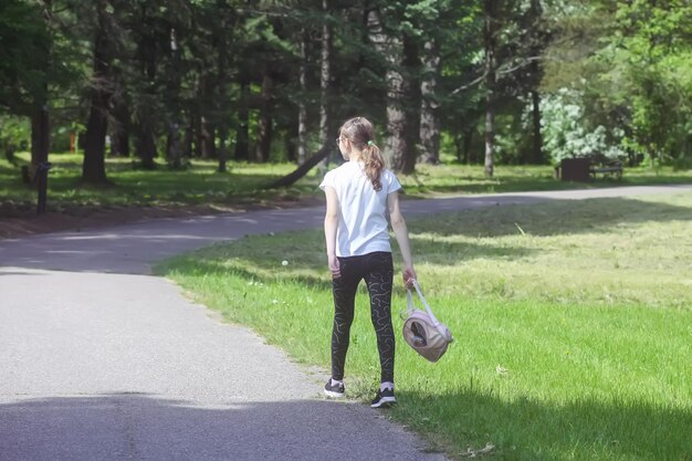 Niña en edad escolar con mochila pequeña camina en el parque de verano