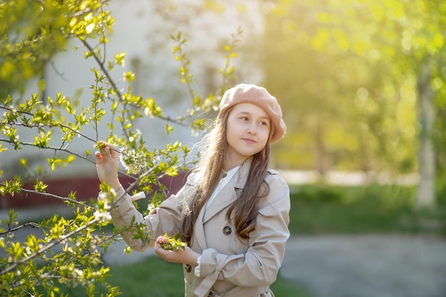 Foto una niña en edad de ir a la escuela primaria está de pie cerca de un árbol en flor y sonríe