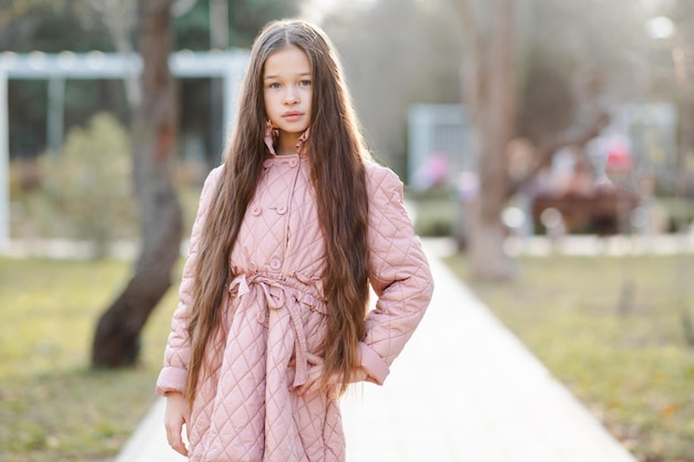 Niña elegante de 1012 años de edad, usa chaqueta con cabello largo y rubio de pie en el parque Temporada de otoño Infancia