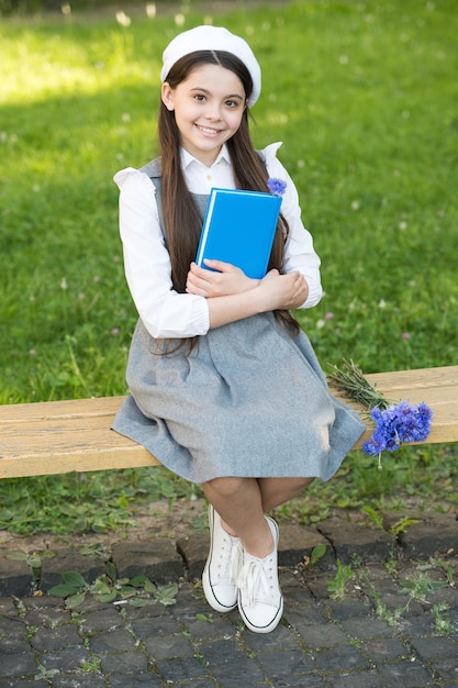 Niña elegante colegiala con libro en libros del parque del concepto de biblioteca