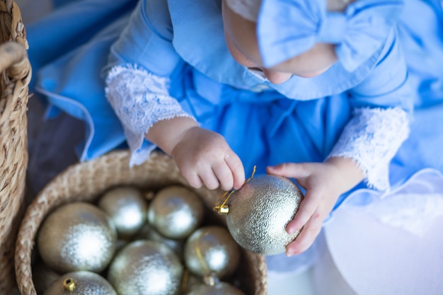 Niña en elegante vestido azul saca la bola de Navidad de la cesta Cesta con juguetes de Año Nuevo