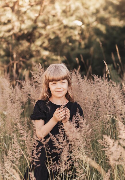 Niña con un elegante vestido negro en la naturaleza en el verano con flores.