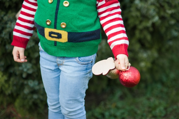 Niña en elf suéter y sombrero esperando una Navidad en el bosque. Retrato de medio cuerpo de un niño pequeño cerca del árbol de navidad